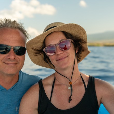 a person wearing sunglasses and smiling next to a body of water