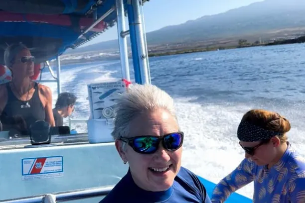 a person wearing sunglasses is sitting on a boat and smiling as the boat moves through the water with the hawaiian sunshine in the background