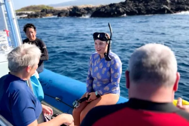 a snorkel guide sits on the side of a zodiak boat with a mask an snorkel on talking to guests on the boat