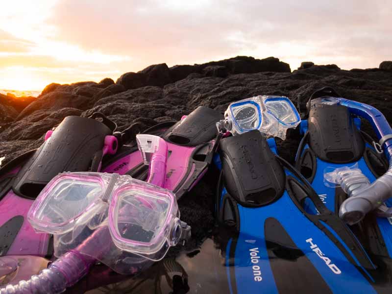 2 sets of snorkeling gear sit on lava rocks with a sunset background