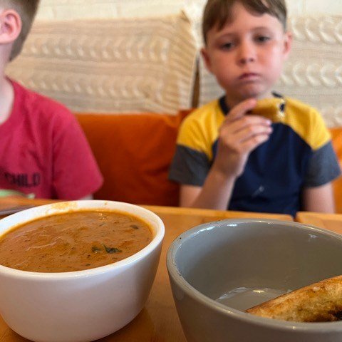 a little boy sitting at a table in front of a bowl of soup