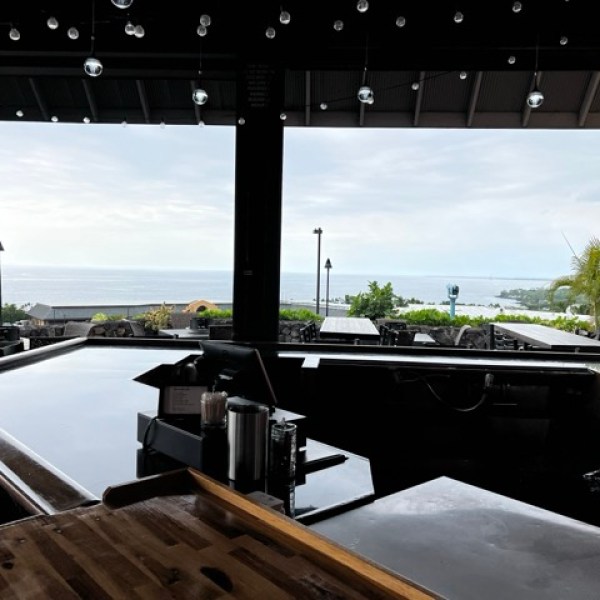 an empty bar with a view of the ocean behind and some seating outside