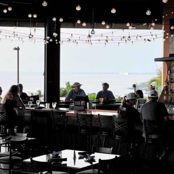 people sit at the bar with a view of the ocean and cruise ship behind