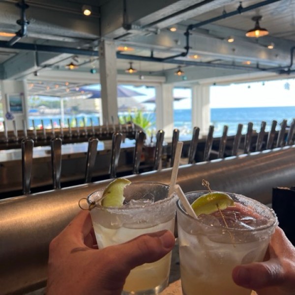 two people cheersing with margaritas in a restaurant bar with an ocean view in the bakcground