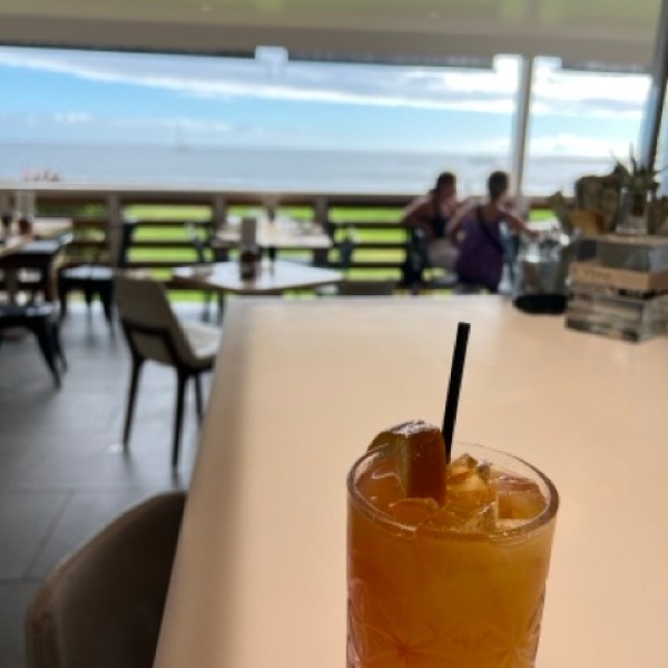a fruity drink in a tumbler on a brighly lit bar with the ocean in the background