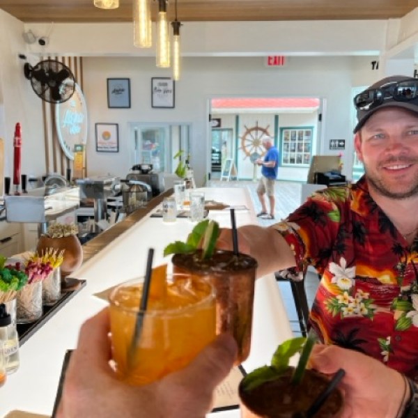 3 people sitting at a brightly lit bar cheersing with drinks
