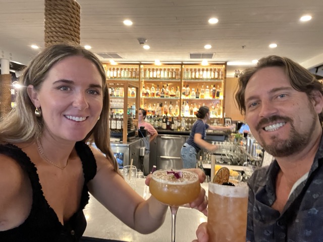 a couple holding drinks with a bar lit up behind