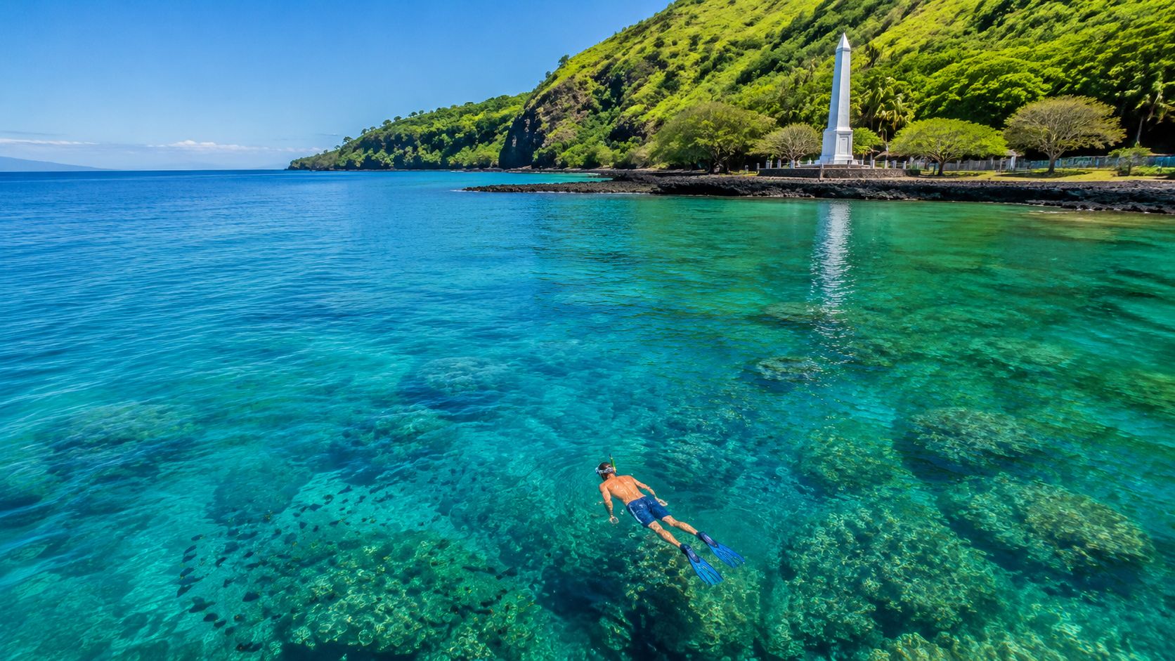 Person snorkeling in clear blue water near a tall white monument on a lush green coast.