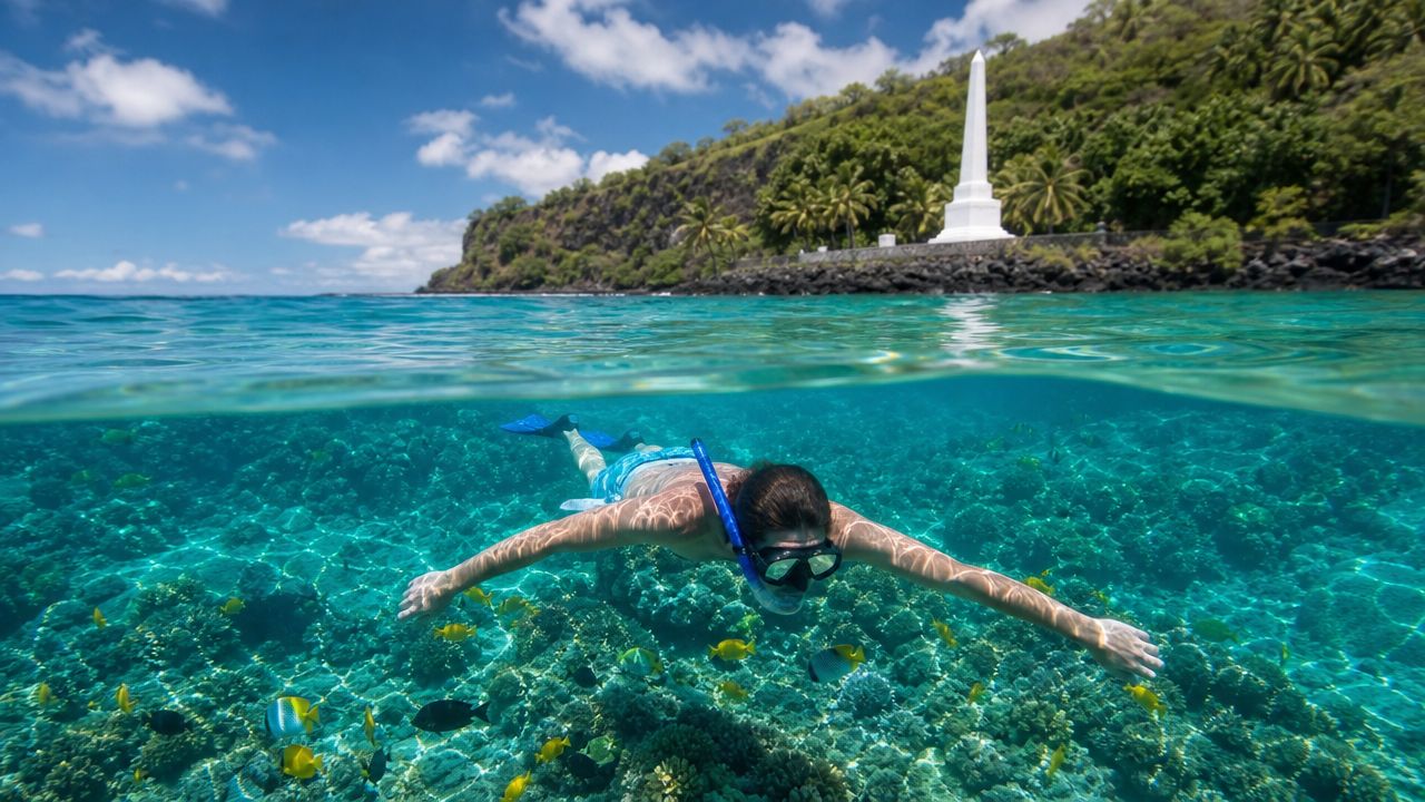Snorkeler swims over coral reef near tropical island with monument.