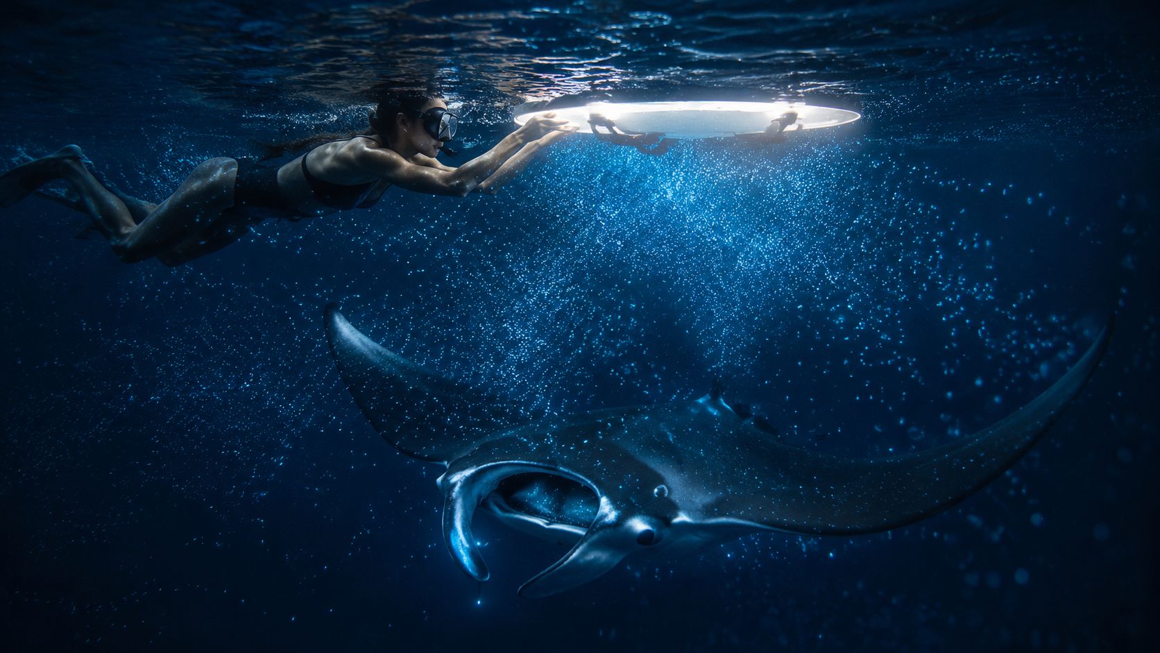 Person swimming underwater with a surfboard near a manta ray.