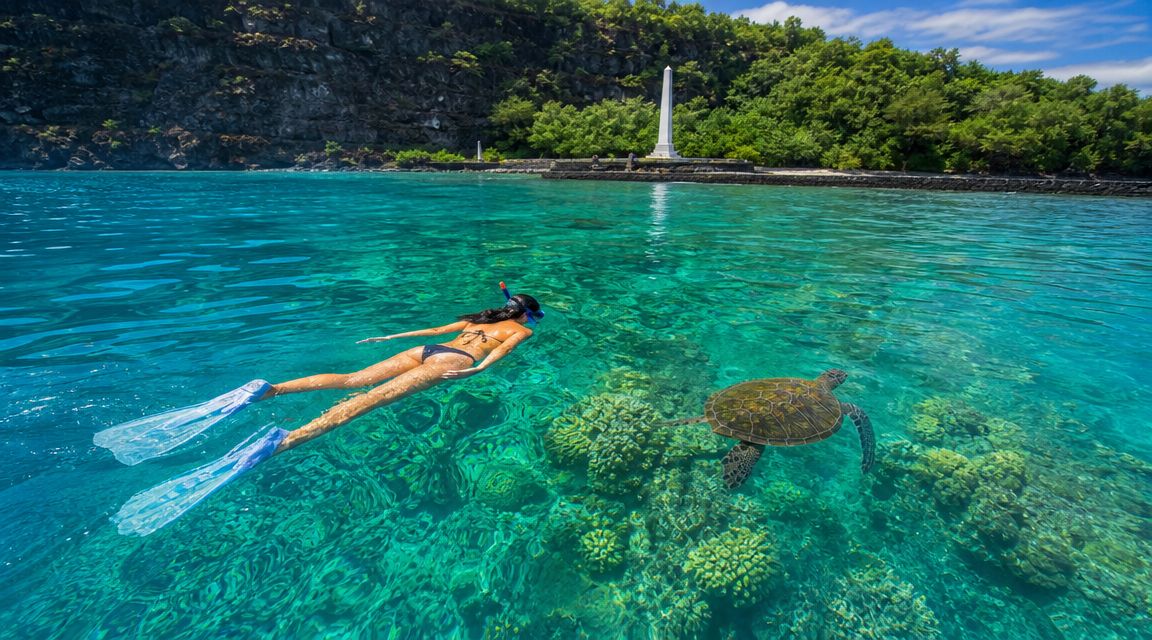 Person snorkeling near a sea turtle in clear waters with a monument in the background.